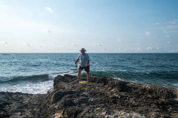 Güneşli bir günde açık mavi gökyüzü ve okyanus dalgalarıyla kayalık sahil şeridinde balıkçılık - açık hava eğlencesi ve deniz aktivitesi