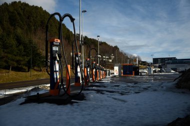 Kışın elektrikli araba şarj istasyonu. Karla kaplı bir otoparkta, ağaçlar, gökyüzü, araba yok. Aalesund, Norveç - 17 Şubat 2024