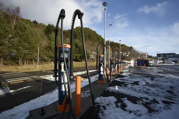 Kışın elektrikli arabalar için şarj istasyonu. Karla kaplı bir otoparkta, ağaçlar, gökyüzü, araba yok. Aalesund, Norveç - 17 Şubat 2024