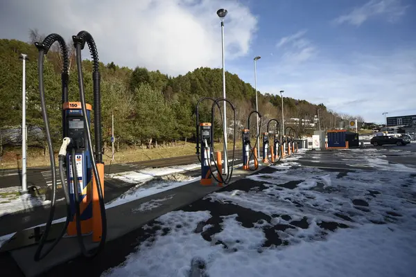 Kışın elektrikli arabalar için şarj istasyonu. Karla kaplı bir otoparkta, ağaçlar, gökyüzü, araba yok. Aalesund, Norveç - 17 Şubat 2024