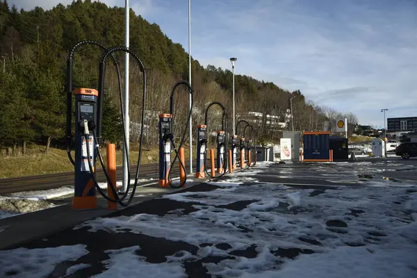 Kışın elektrikli arabalar için şarj istasyonu. Karla kaplı bir otoparkta, ağaçlar, gökyüzü, araba yok. Aalesund, Norveç - 17 Şubat 2024