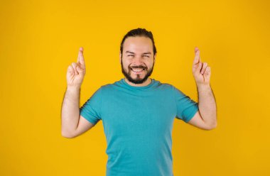 Portrait of young hispanic man with positive energy and fingers crossed on yellow background in Mexico Latin America