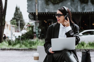 Young hispanic businesswoman working using laptop sitting on the bench in Mexico city in Latin America