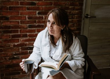 Hispanic senior mature woman reading a book in pijama at home in Mexico Latin America