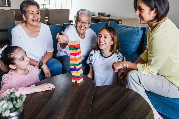 Hispanic family playing Jenga game with grandmother and daughter at home, three generations of women in Mexico Latin America
