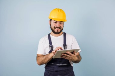 portrait of Hispanic bearded young man engineering and worker with hard helmet in Mexico Latin America on blue background