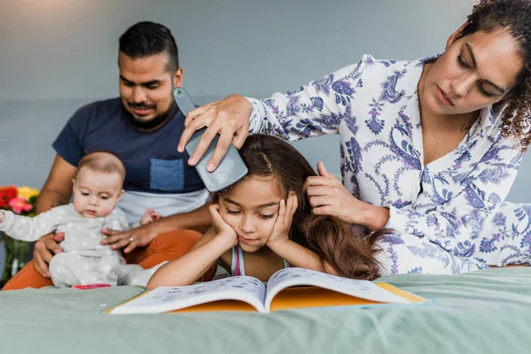 hispanic family reading a book while mother comb the hair of daughter on the bed at home in Mexico Latin America