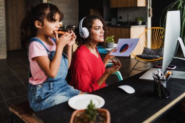 Hispanic mother working in a video conference at home while she takes care of her daughter in Mexico Latin America, home office concept