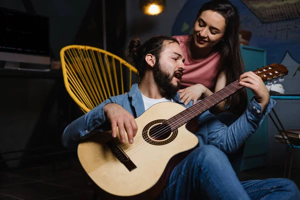 Hispanic couple playing guitar, Girlfriend and boyfriend having fun at home at night in Mexico Latin America