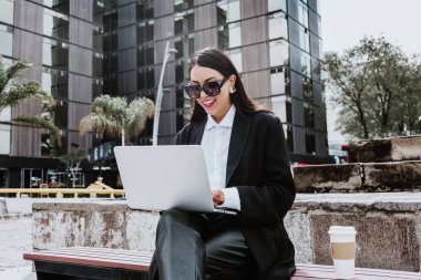 Young hispanic businesswoman working using laptop sitting on the bench in Mexico city in Latin America