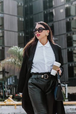 young hispanic business woman walking on the street holding coffee and looking sideways in Mexico city in Latin America