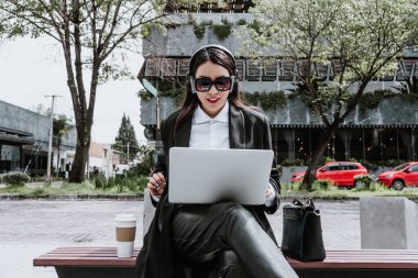 Young hispanic businesswoman working using laptop sitting on the bench in Mexico city in Latin America