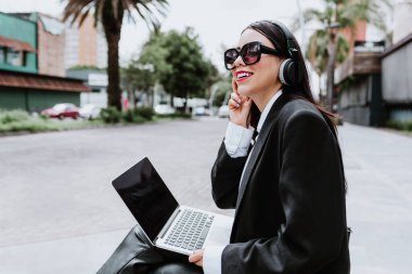 Young hispanic businesswoman working using laptop sitting on the bench in Mexico city in Latin America