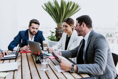 Group of hispanic business people in a informal meeting using laptop on the terrace of the office in Mexico Latin America, teamwork working