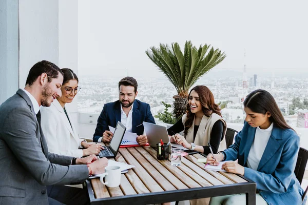Group of hispanic business people in a informal meeting using laptop on the terrace of the office in Mexico Latin America, teamwork working