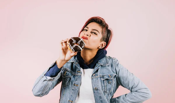 stock image young hispanic woman on disagreement with eat donuts or junk food on coral pink background in Mexico Latin America