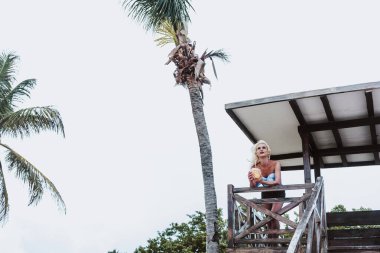 Meksika 'da Latin Amerika plajında makyaj yapan transseksüel bir adamın portresi ve elinde hindistan cevizi tutan kadın giysileri.