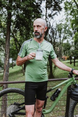hispanic Senior man drinking water or energy drink on his mountain bike outdoors in Mexico Latin America