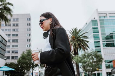 Latin kökenli genç bir iş kadını elinde kahveyle sokakta yürüyor ve Mexico City 'de yan bakıyor, İspanyol bir kadın.