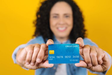 hispanic adult adult woman holding blue credit card isolated over yellow background in Latin America