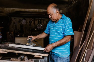 Latin kıdemli marangoz, Meksika Latin Amerika 'da bir atölyede cilalanmış bir ahşap üzerinde zımpara kağıdı kullanıyor.