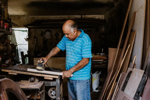 stock image latin senior man carpenter using sandpaper on a polished wood in workshop in Mexico Latin America