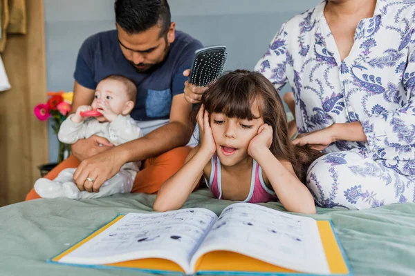 Familia Latina Leyendo Libro Mientras Madre Peina Cabello Hija Cama — Foto de Stock