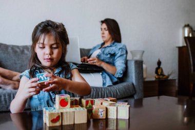 Latin bir kız çocuğu Meksika 'da evinde tuğlalarla oynuyor. Ailesi de arka planda, İspanyol insanlar.