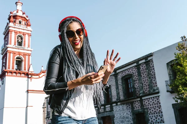 在墨西哥的街上 留着辫子 头戴耳机和手机听音乐的年轻拉丁女人和他的惊慌失措的人们 — 图库照片