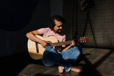 Latin adam akustik gitar çalıyor. Oturma odasında yerde oturuyor. Sunny 'nin sert ışığı Meksika' da Latin Amerika 'daki Stylish Loft Apartmanı' nda.