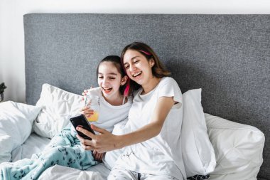 Latin genç kız kardeşler Meksika 'da evde telefonla yatakta yatıyorlar. Latin kökenli kadın aile.