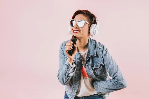 young latin woman girl listening music with headphones  and holding mobile phone on coral pink background with copy space studio portrait in Mexico Latin America, hispanic people