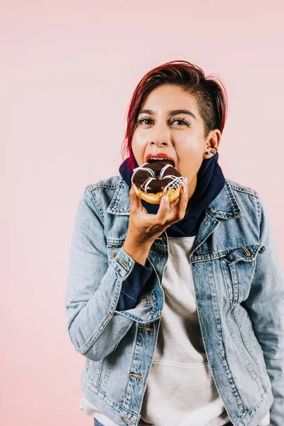 young latin woman eating chocolate donuts on coral pink background in Mexico Latin America, hispanic people