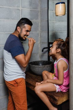 Latin genç bir baba kızına Meksika 'da dişlerini nasıl fırçalayacağını öğretiyor.