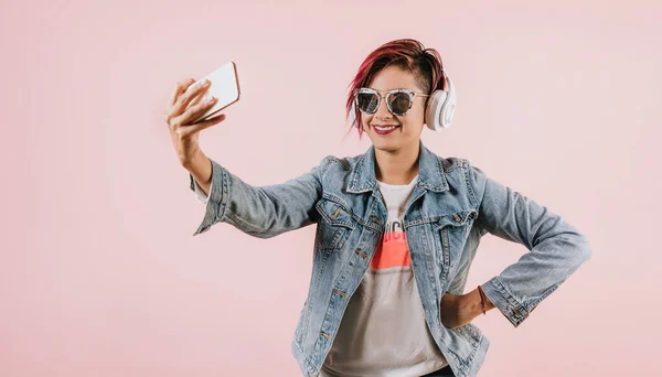 young latin woman listening music with headphones and holding mobile phone on coral pink background with copy space studio portrait in Mexico Latin America, hispanic female