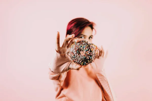 young latin woman eating chocolate donuts on coral pink background in Mexico Latin America, hispanic people   with junk food