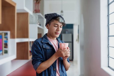 Latin homoseksüel bir adam elinde çay bardağıyla Meksika 'nın penceresinin yanında rahatlıyor. Latin Amerika' nın lgbtq bölgesinden İspanyol asıllı insanlar.