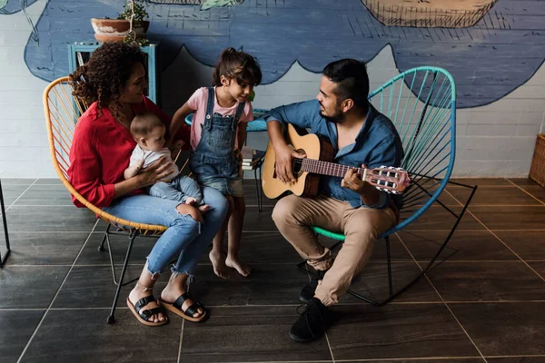 latin father playing guitar, singing and having fun with his family wife baby and daughter at home in Mexico Latin America, hispanic people