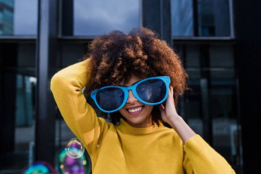 Latin Amerika şehrinde canlı güneş gözlüğü takan genç Afro-Amerikalı kadın, Latin ve Karayipli kadın, parti karnavalı için afro saçlı 