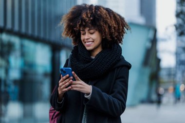 Latin Amerika şehrinde cep telefonu kullanan genç Afrikalı Amerikalı iş kadını, gökdelen geçmişe sahip İspanyol finans ve Karayipliler