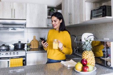 Latin yetişkin bir kadın Meksika 'da mutfakta kahvaltıda portakal suyu içiyor. Latin bir kadın.