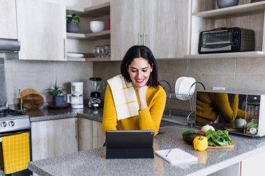 Latin yetişkin kadın sağlıklı yemekler pişiriyor ve Meksika Latin Amerika 'da evdeki mutfakta dijital tablet tutuyor.