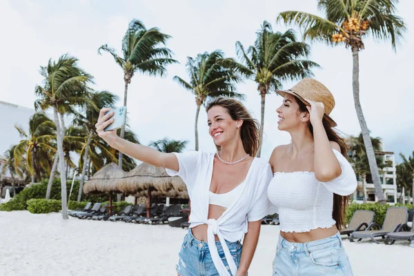 young latin woman taking photo selfie with mobile phone to female friend at caribbean beach in Mexico Latin America, hispanic female