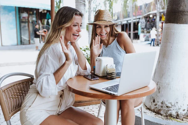 young latin couple of women friends using laptop and drinking coffee at restaurant terrace for video conference in Mexico Latin America, hispanic people in caribbean city with tropical background