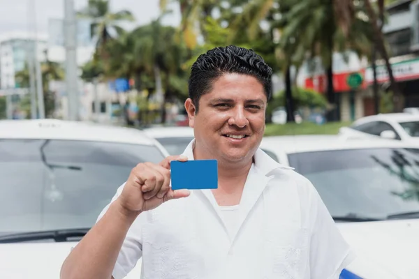 portrait of latin taxi driver man holding blank card with car on background at city street in Mexico in Latin America, Hispanic adult people