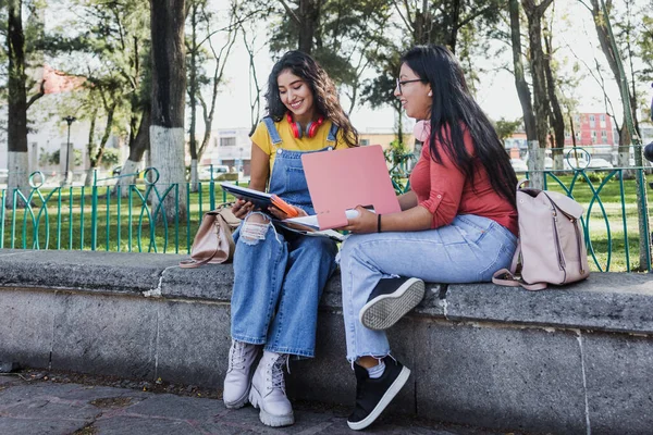 portrait of young latin women or university students using mobile phone in Mexico Latin America, hispanic girls studying outdoors in public park