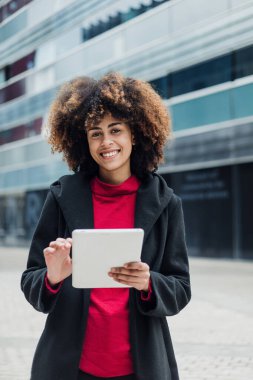 Latin Amerika şehrinde dijital tablet kullanan genç Afrikalı Amerikalı iş kadını, gökdelen geçmişe sahip İspanyol finans ve Karayipliler