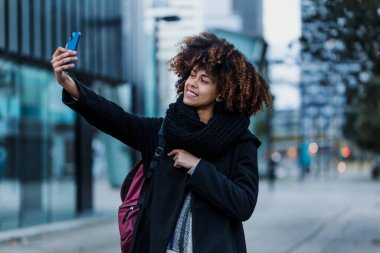Latin Amerika şehrinde cep telefonuyla fotoğraf çeken genç Afrikalı Amerikalı iş kadını İspanyol ve Karayipliler gökdelen geçmişli.