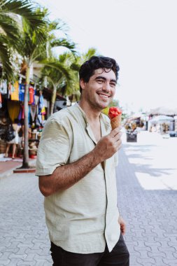 hispanic young man eating ice cream on vacations or holidays in Mexico Latin America, Caribbean and tropical destination clipart