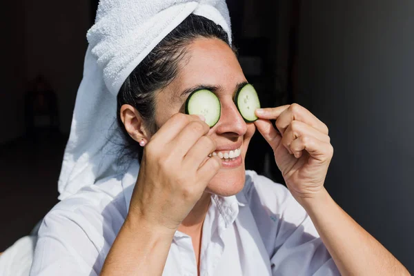 Latin adult woman applying facial mask on face with cucumber slices for exfoliation at home in Mexico Latin America, hispanic people